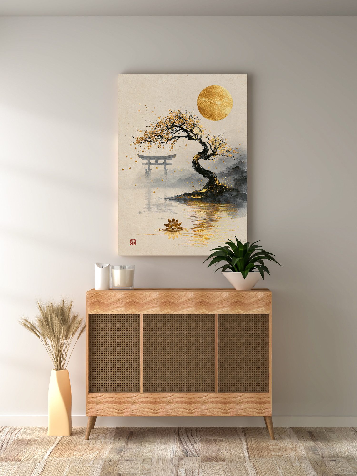 Golden Moon Over the Old Sakura: an old cherry tree leans over a still lake under a full gold moon, golden blossoms falling toward the water. A torii gate stands in the mist across the lake, and a single golden lotus floats near the bottom. A red seal sits in the lower left. The print hangs above a wooden cabinet with rattan doors. A plant in a white bowl on the cabinet reaches in front of the print's lower corner, next to candles. Dried grass in a tall vase stands on the floor to the left.